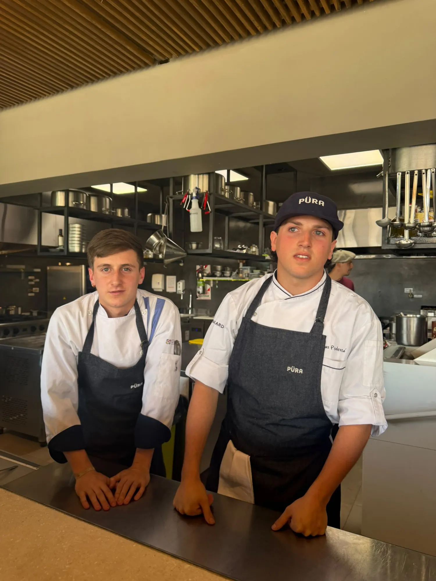 José “Coké” Nallib and Tomás Podestá in Püra aprons, leaning on the pass in the winery kitchen