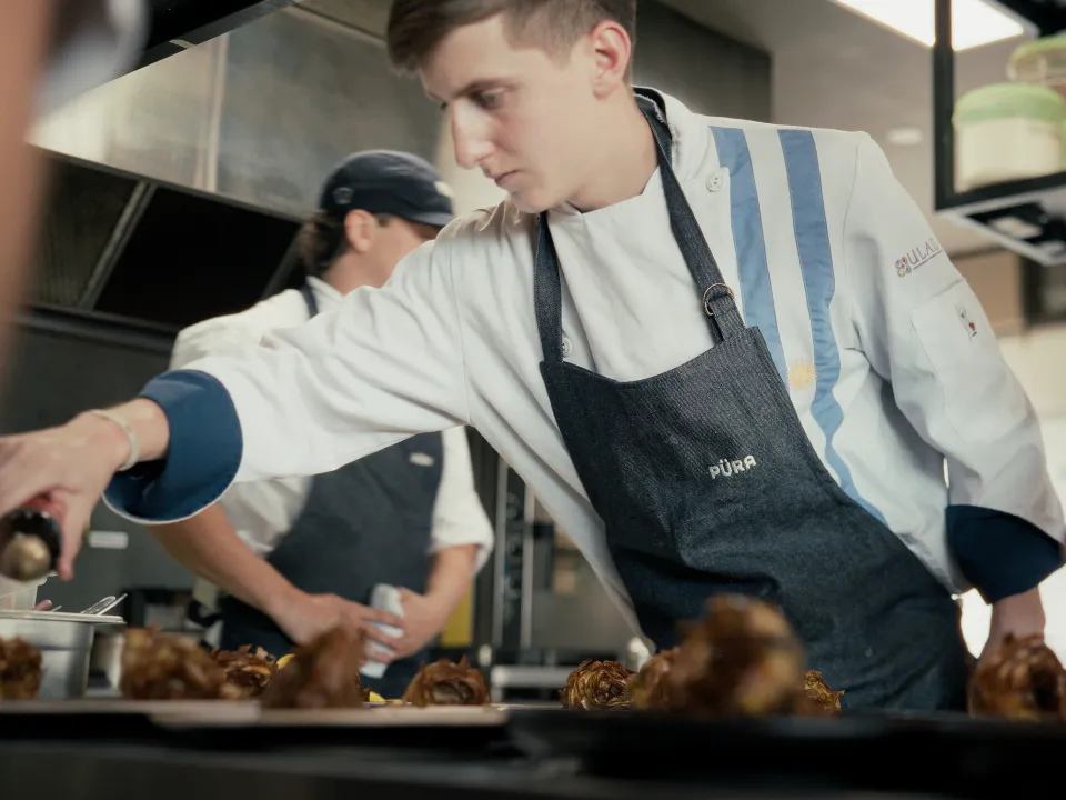 José “Coké” Nallib drizzling olive oil over the artichokes, in chef whites and a Püra apron